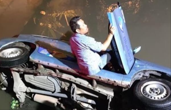 Sopir dan taxi blue bird nyemplung ke sungai di belakang Poltek Sriwijaya, Minggu (12/11/2023). Foto : Screenshot medsos.