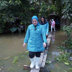 Ketua TP PKK Kota Palembang, Dewi Sastrani Ratu Dewa melewati jalan banjir menuju rumah warga 15 Ulur yang sakit, Kamis (13/3/2025). Foto: Kominfo Palembang.
