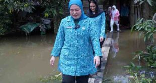 Ketua TP PKK Kota Palembang, Dewi Sastrani Ratu Dewa melewati jalan banjir menuju rumah warga 15 Ulur yang sakit, Kamis (13/3/2025). Foto: Kominfo Palembang.