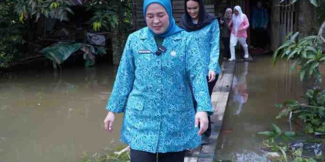 Ketua TP PKK Kota Palembang, Dewi Sastrani Ratu Dewa melewati jalan banjir menuju rumah warga 15 Ulur yang sakit, Kamis (13/3/2025). Foto: Kominfo Palembang.