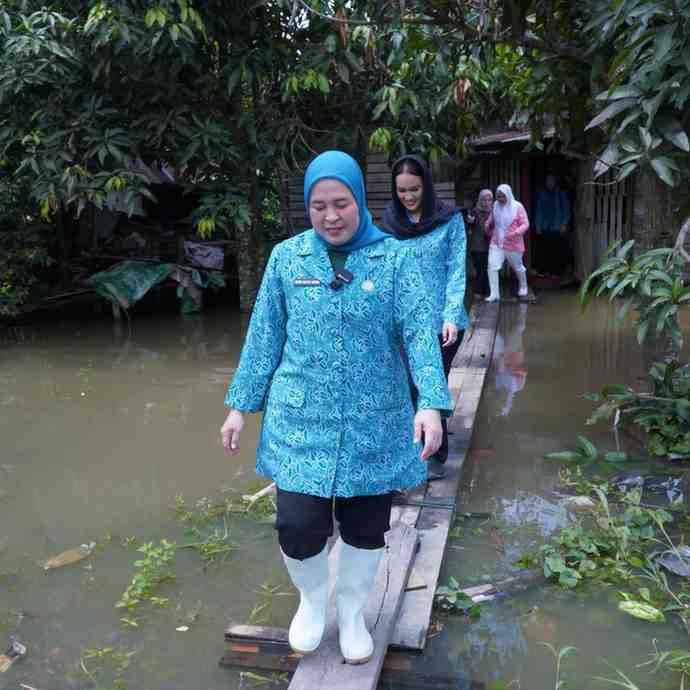 Ketua TP PKK Kota Palembang, Dewi Sastrani Ratu Dewa melewati jalan banjir menuju rumah warga 15 Ulur yang sakit, Kamis (13/3/2025). Foto: Kominfo Palembang.