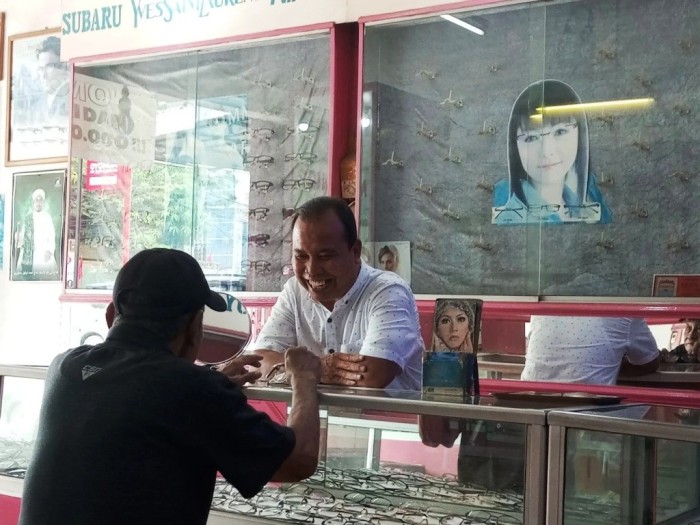 Uda Andi, Owner Optik Sriwijaya, sedang melayani pelanggan yang datang untuk membeli kacamata. (SUMSELHEADLINE.COM/OYONG)
