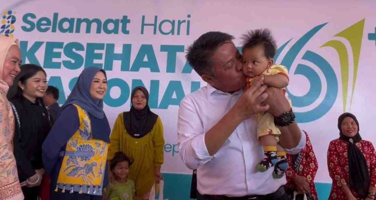 Gubernur Sumsel, Herman Deru menggendong bayi pada peringatan Hari Kesehatan Nasional (HKN) ke-61 di Desa Merah Mata, Kecamatan Banyuasin I, Kamis (27/11/2025). Foto: Humas Pemprov Sumsel.